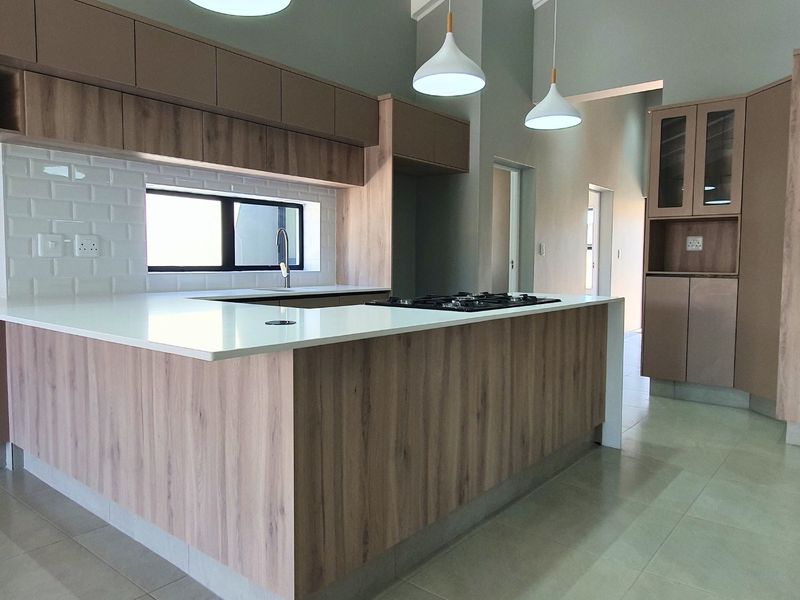 Modern kitchen featuring wood-finish cabinetry, stone countertops, a gas hob, subway tile backsplash, and contemporary pendant lighting in an open-plan layout.