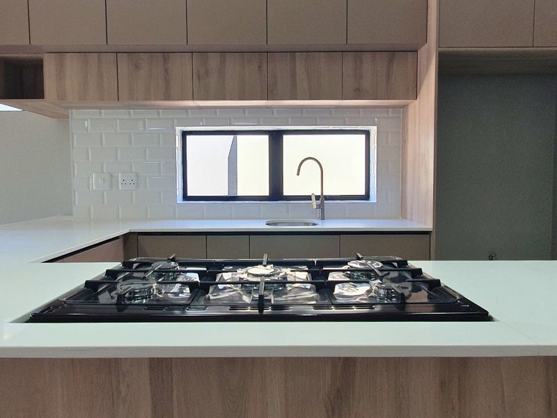 Modern kitchen featuring light wood cabinetry, stone countertops, a built-in gas hob, and a subway tile backsplash with a sleek undermount sink.