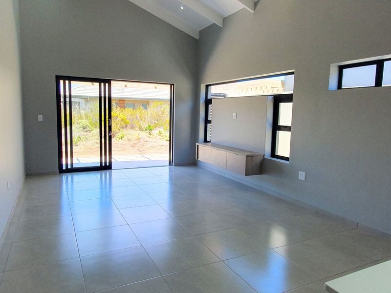 Spacious, modern living area featuring high vaulted ceilings, large sliding glass doors, and a sleek built-in media console with neutral tiled flooring.