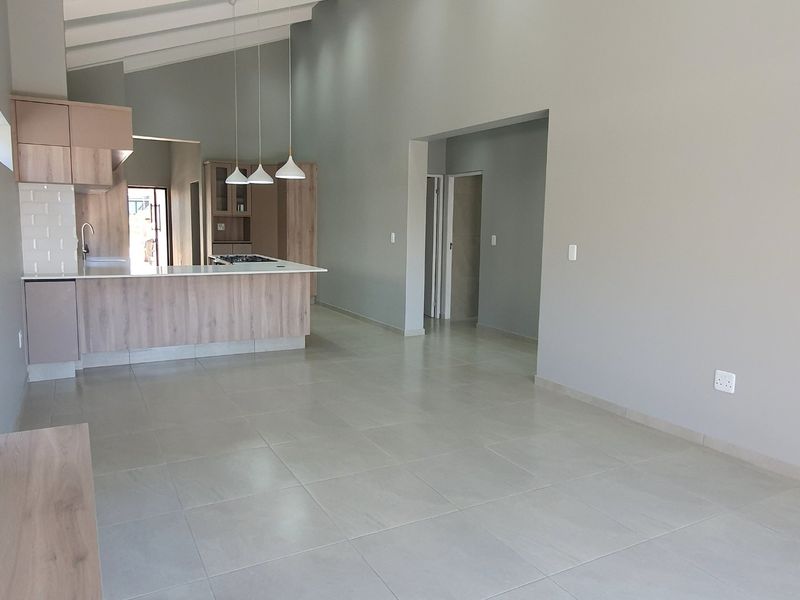 Spacious open-plan living and kitchen area featuring modern cabinetry, a kitchen island, vaulted ceilings, and neutral tiled flooring throughout.