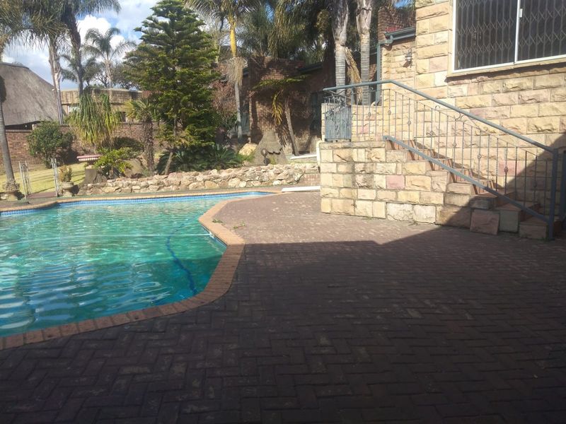 Outdoor pool area featuring brick paving, stone-clad retaining walls, and a metal staircase leading to the upper level of the house.