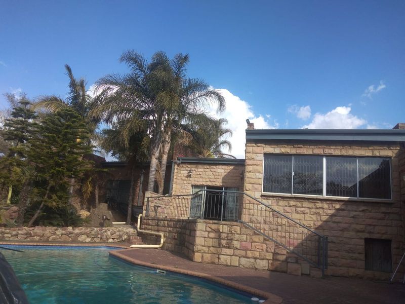 Rear exterior view featuring a swimming pool, stone-clad building facade, paved pool deck, and metal security features.