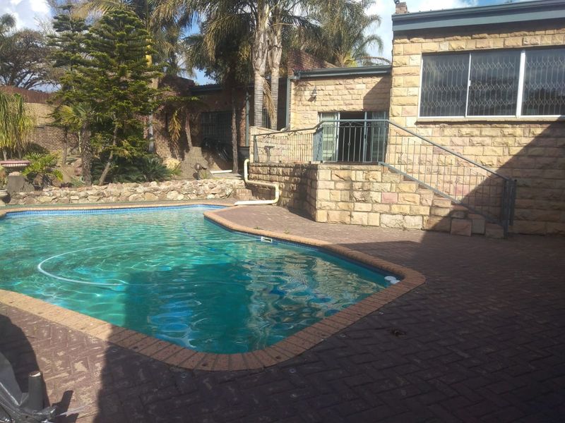 Outdoor pool area featuring a paved patio, stone-clad exterior walls, and a swimming pool with surrounding stone retaining walls and landscaping.