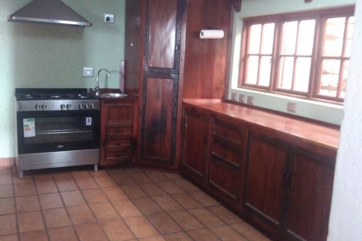 A functional kitchen featuring wooden cabinetry, tiled flooring, and a stainless steel extractor fan with a freestanding oven.