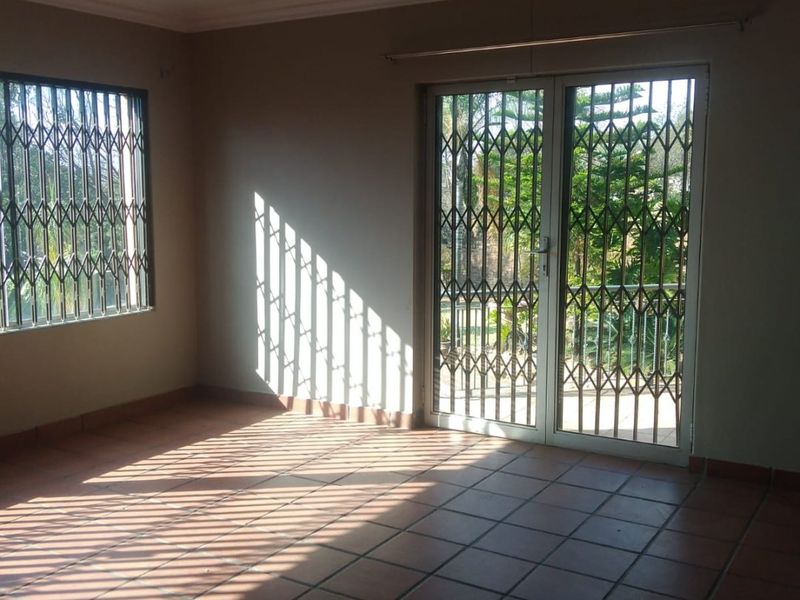 An empty living room featuring terracotta-style floor tiles, coved ceilings, and security gates on the windows and sliding glass doors leading to the garden.