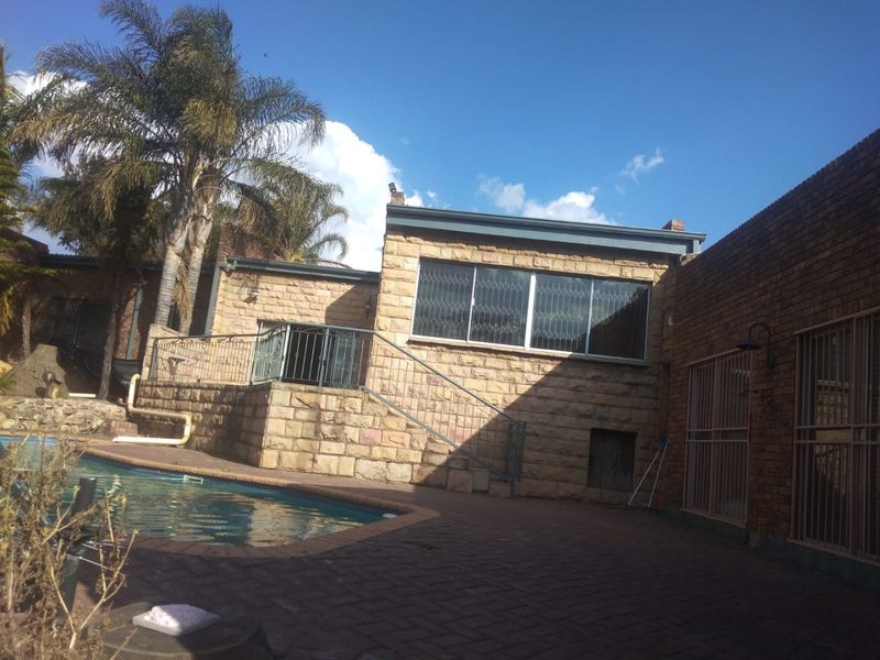 Rear exterior view of the property featuring a swimming pool, stone-clad facade, and paved patio area with security features.