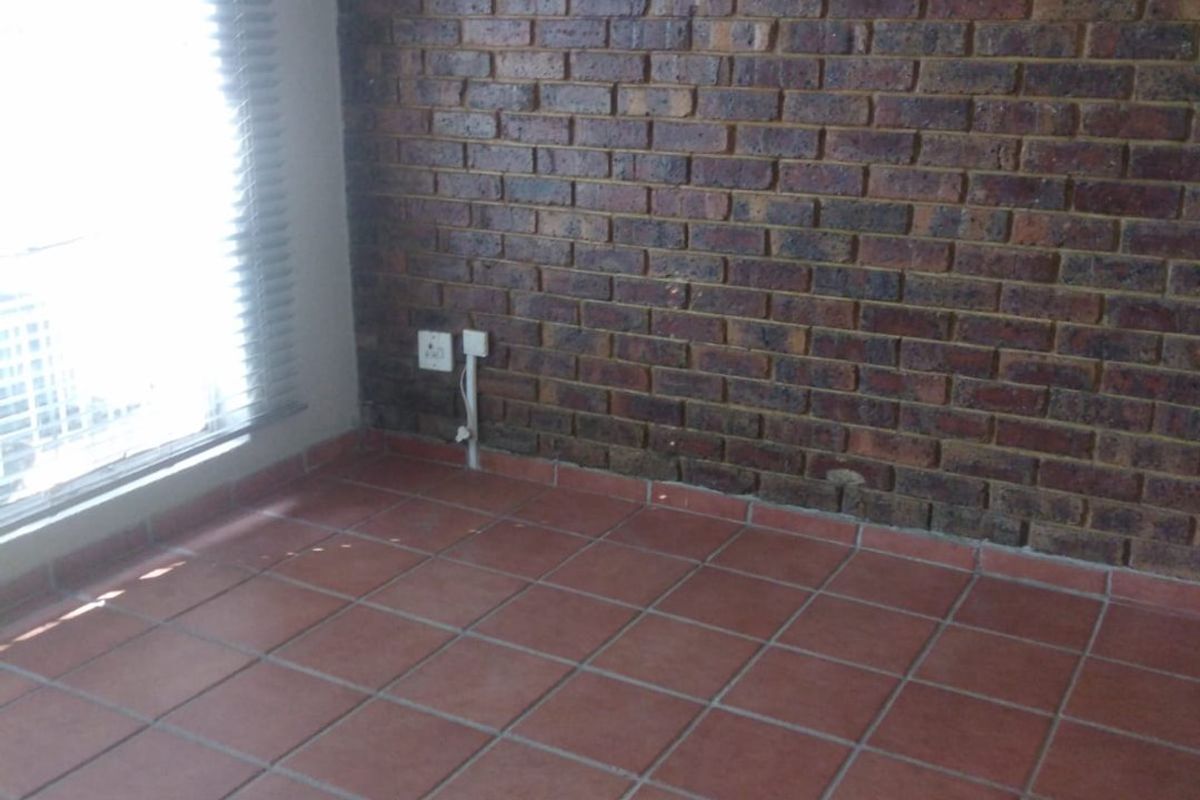 An empty bedroom featuring a rustic exposed brick wall, terracotta floor tiles, and natural light through venetian blinds.