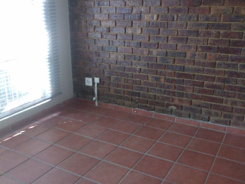 An empty bedroom featuring a rustic exposed brick wall, terracotta floor tiles, and natural light through venetian blinds.