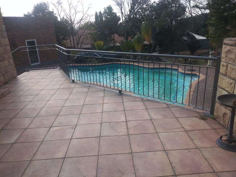 Outdoor tiled patio area overlooking a swimming pool, featuring a wrought iron safety balustrade and stone-clad exterior walls.