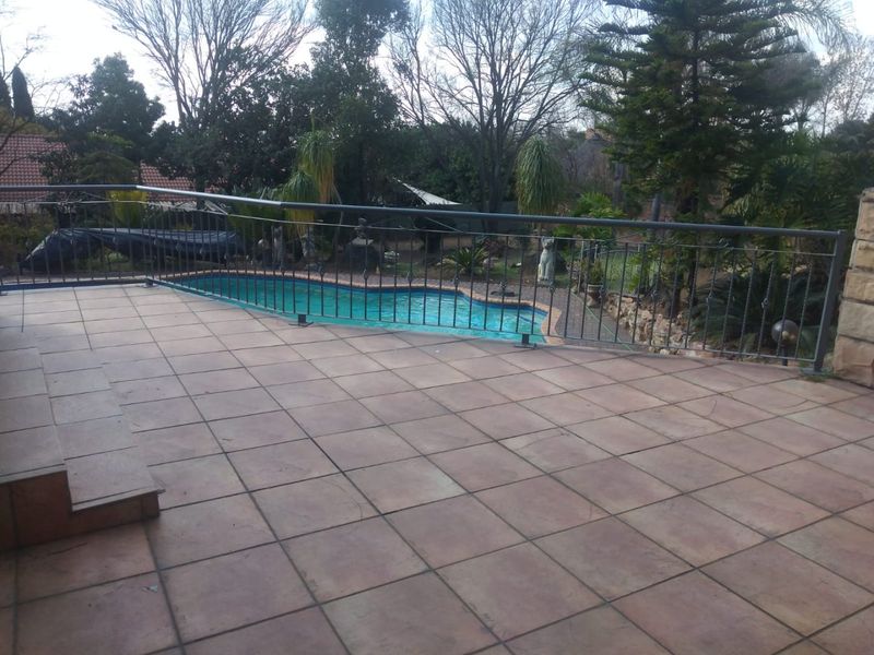 Spacious tiled patio area featuring a metal balustrade overlooking a private swimming pool and established garden.