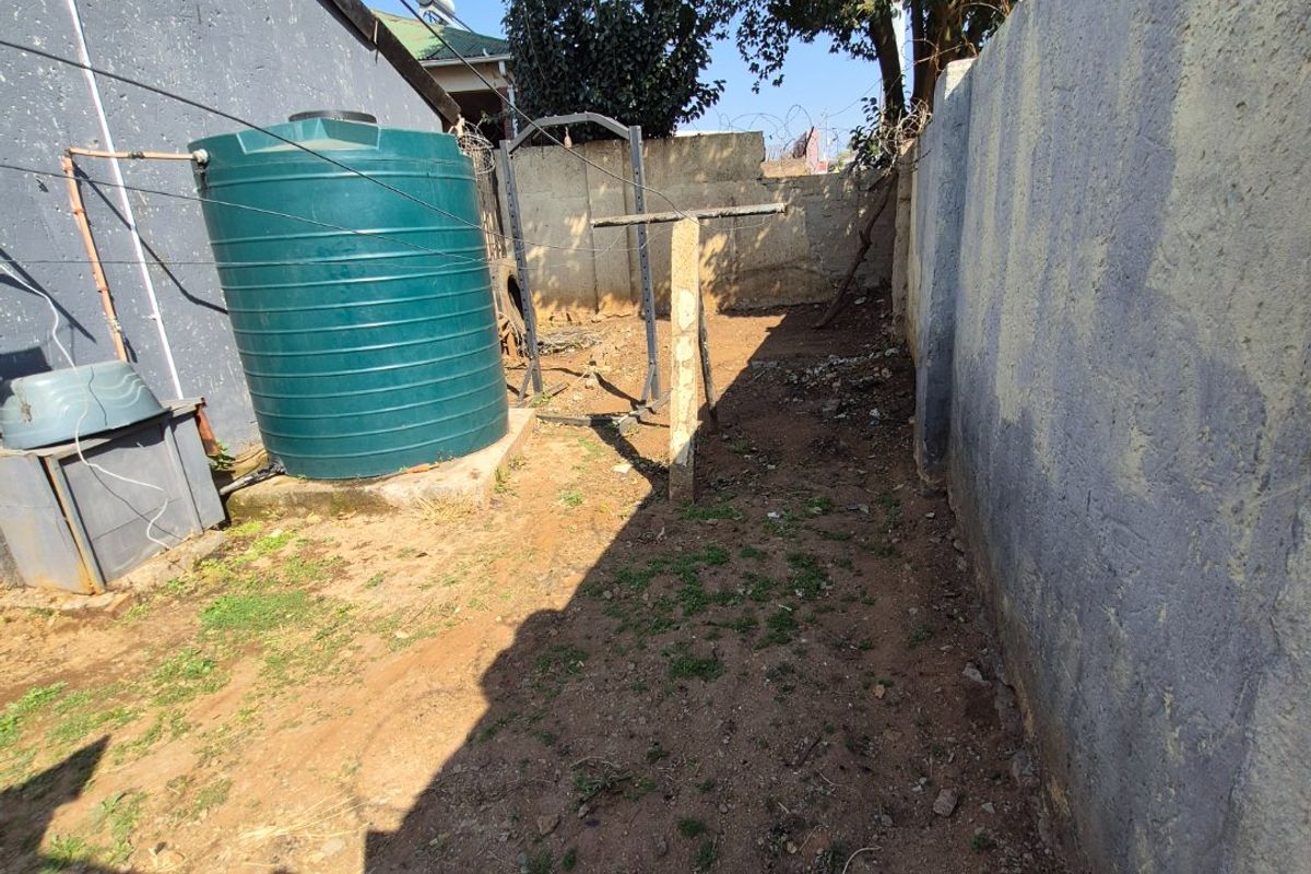 A narrow rear exterior side yard featuring a large water storage tank, perimeter boundary walls with security wire, and an unpaved ground surface.