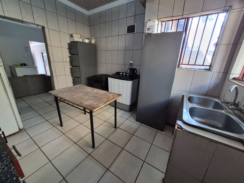 A functional kitchen area featuring tiled walls and flooring, a double bowl stainless steel sink, and security bars on the window.