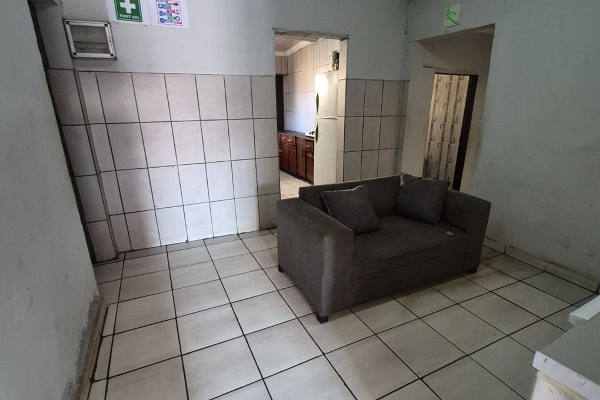 A living area featuring tiled flooring and wall cladding with visible signs of wear and wall cracks requiring maintenance.