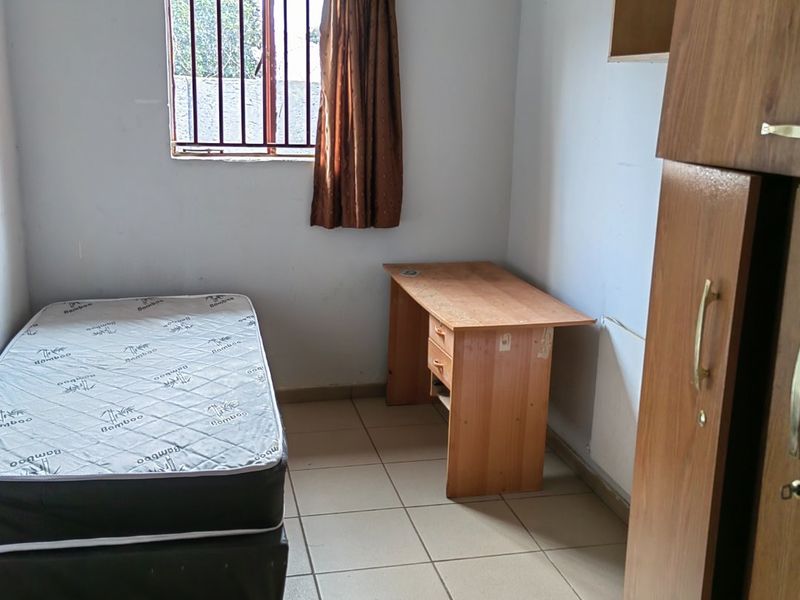 A functional bedroom featuring ceramic floor tiles, a window with security burglar bars, and built-in shelving units.