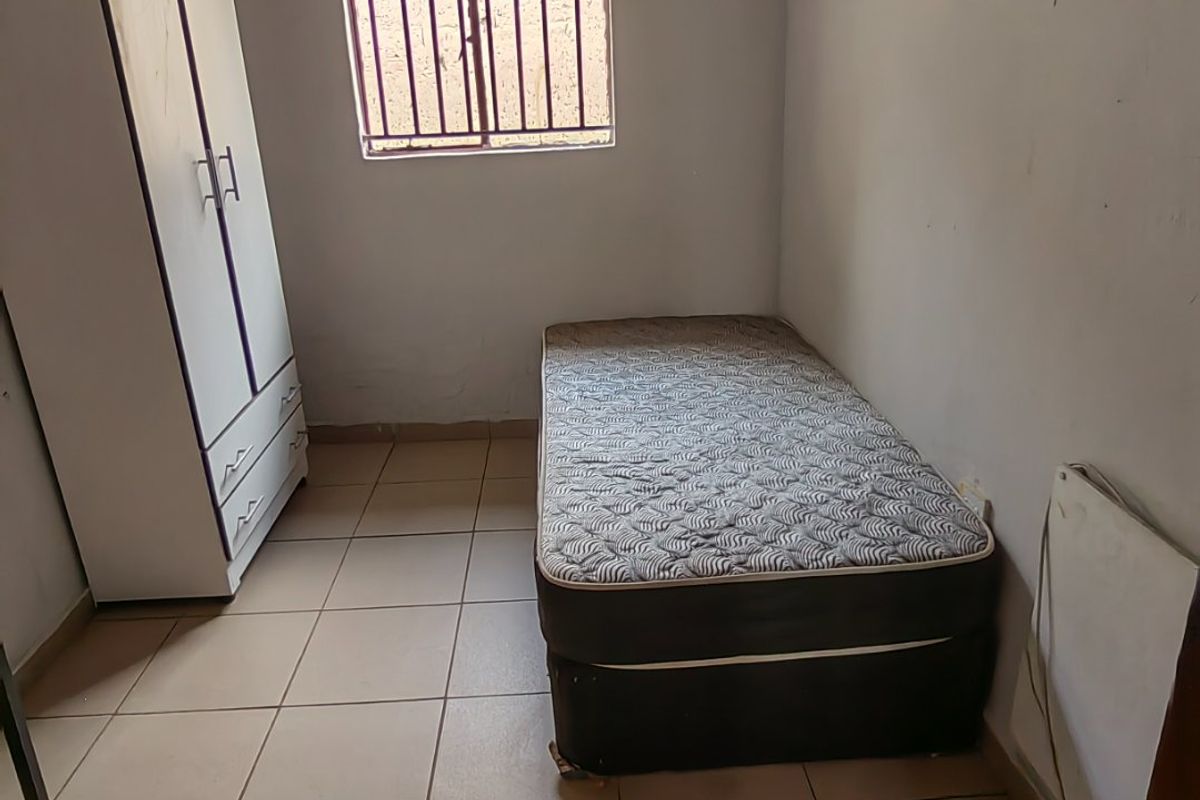 A compact bedroom featuring tiled flooring, security bars on the window, and built-in shelving, requiring cosmetic updates to the walls and ceiling.