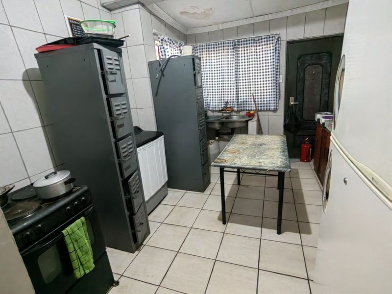 A functional kitchen space featuring tiled walls and flooring, equipped with a double sink and freestanding stove, requiring ceiling repairs and cosmetic updates.