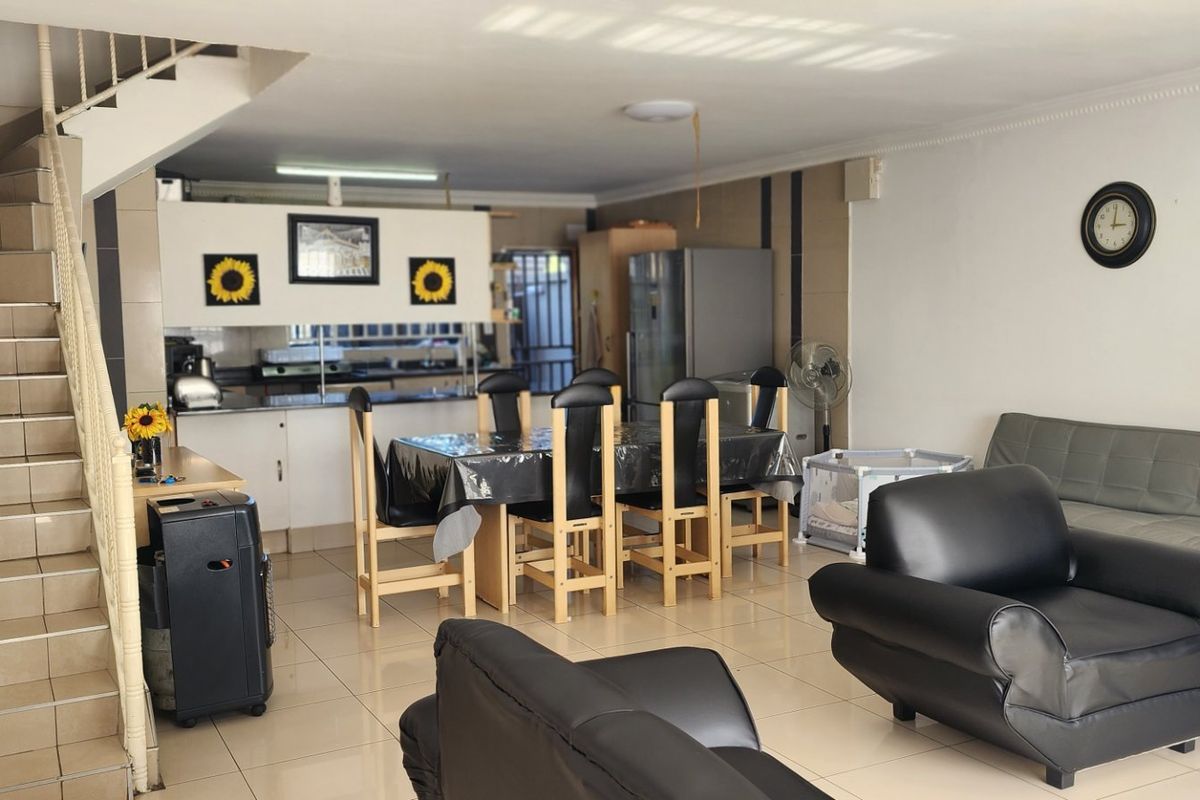 Open-plan living and dining area featuring tiled flooring, a staircase with metal balustrade, and an integrated kitchen space.