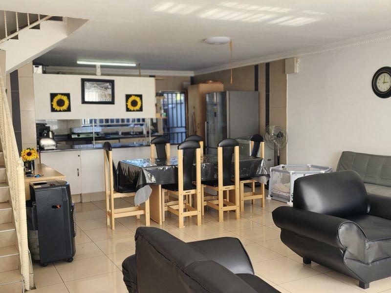 Open-plan living and dining area featuring tiled flooring, a staircase with metal balustrade, and an integrated kitchen space.