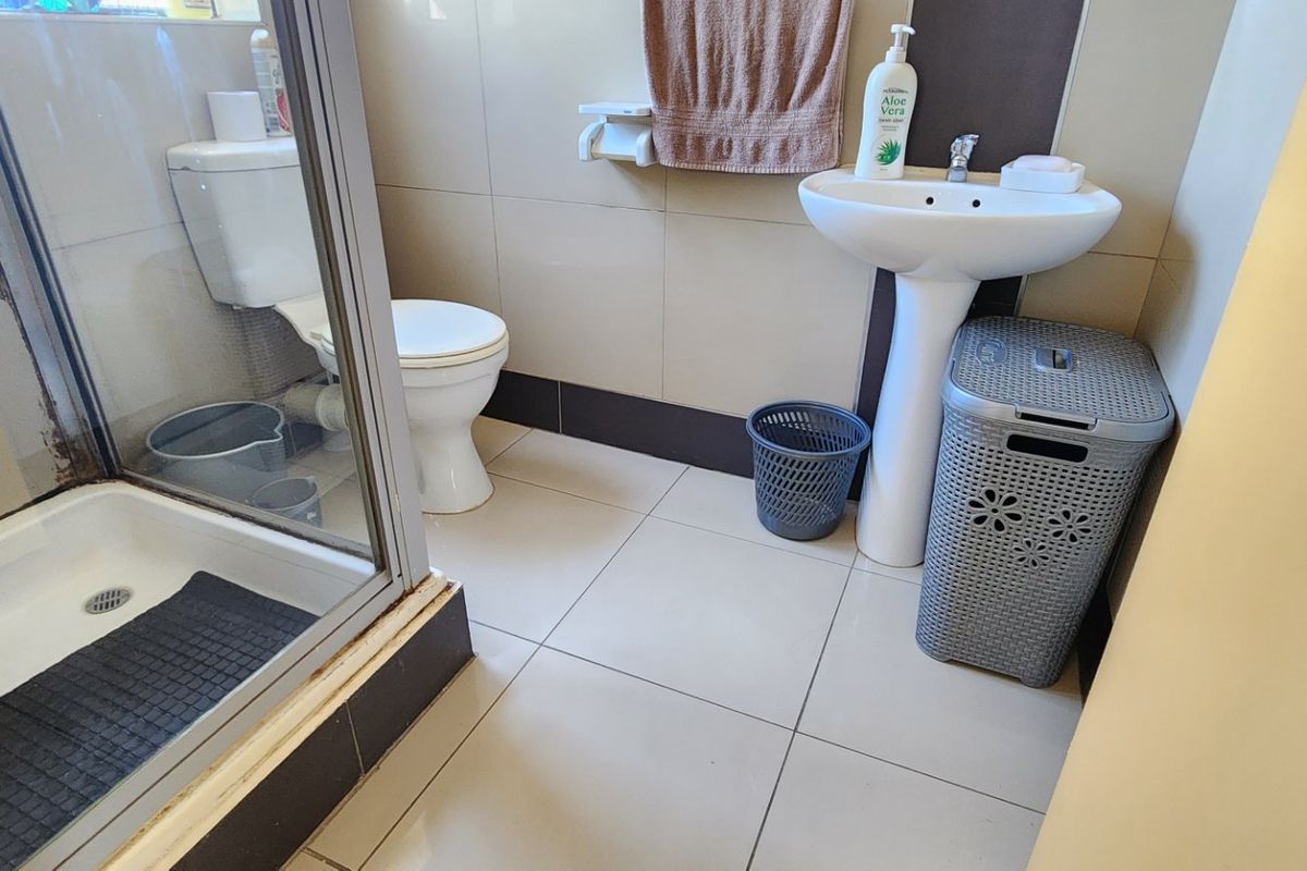 A functional bathroom featuring a pedestal basin, toilet, and a glass-enclosed shower with tiled walls and flooring.