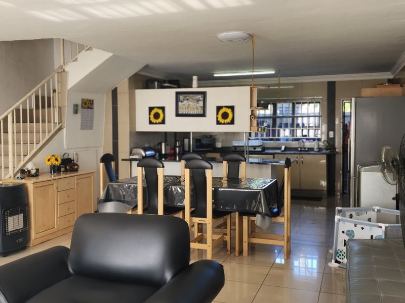 Open-plan living and dining area featuring tiled flooring and an integrated kitchen with built-in cabinetry, adjacent to an internal staircase.