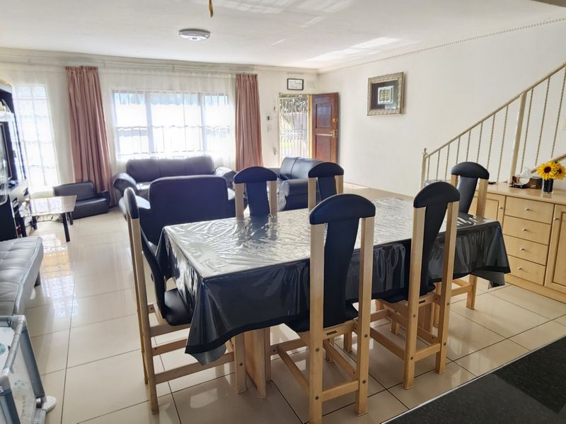Spacious open-plan living and dining area featuring tiled flooring, a staircase with metal railing, and built-in cabinetry, offering a functional layout for daily living.