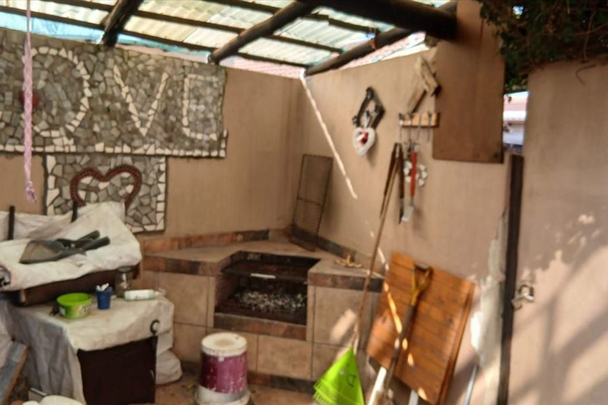 Covered outdoor patio area featuring a built-in braai, tiled prep surfaces, and a translucent roof structure, requiring some maintenance and cosmetic updates.