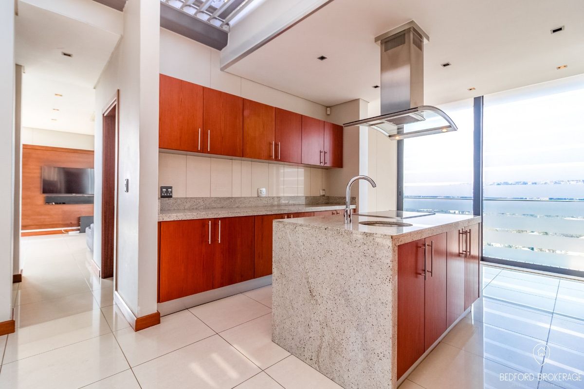 Modern kitchen featuring granite countertops, a central island with an integrated sink, stainless steel extractor fan, and ample built-in cabinetry with a view.