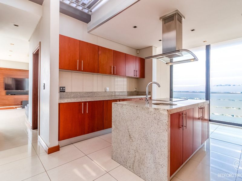 Modern kitchen featuring granite countertops, a central island with an integrated sink, stainless steel extractor fan, and ample built-in cabinetry with a view.