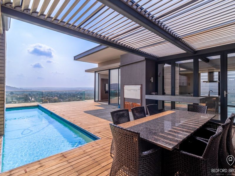 Spacious covered balcony featuring timber decking, a private swimming pool, built-in braai, and panoramic views, seamlessly connected to the interior living space.