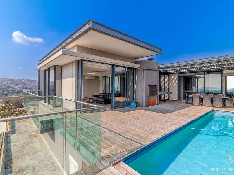 Spacious outdoor terrace featuring a swimming pool, timber decking, glass balustrades, and a built-in braai, offering expansive views.
