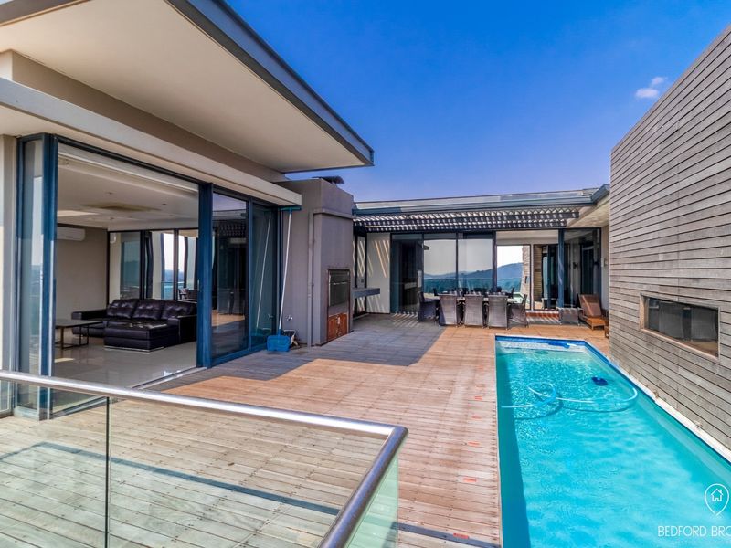 Spacious outdoor entertainment area featuring a swimming pool, timber decking, built-in braai, and seamless flow to the interior living spaces.