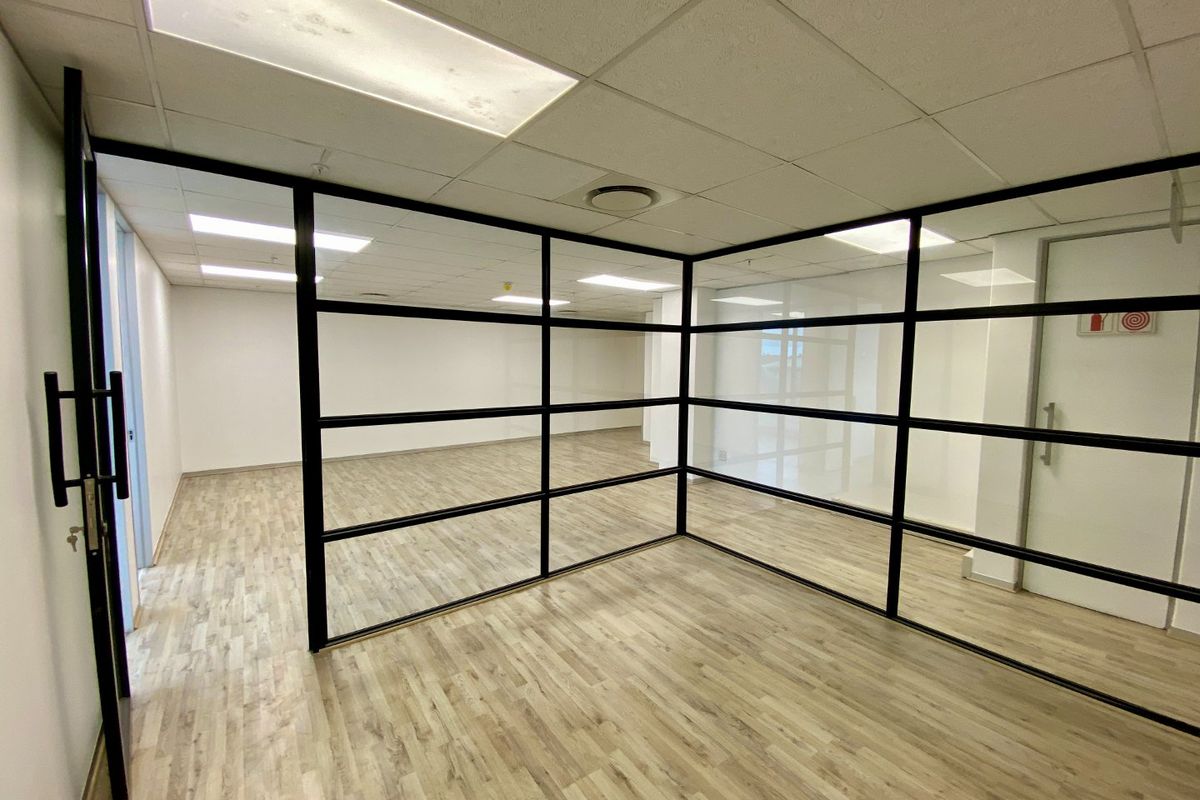 Modern commercial office space featuring clean wood-look flooring, suspended ceiling tiles, and contemporary black-framed glass partitioning for a bright, professional open-plan layout.