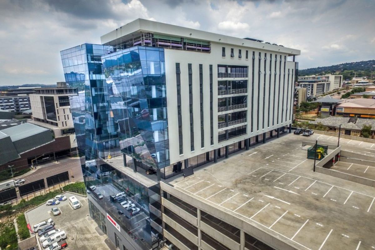 Aerial view of a modern multi-story commercial office building featuring a glass facade and an adjacent multi-level concrete parking structure.
