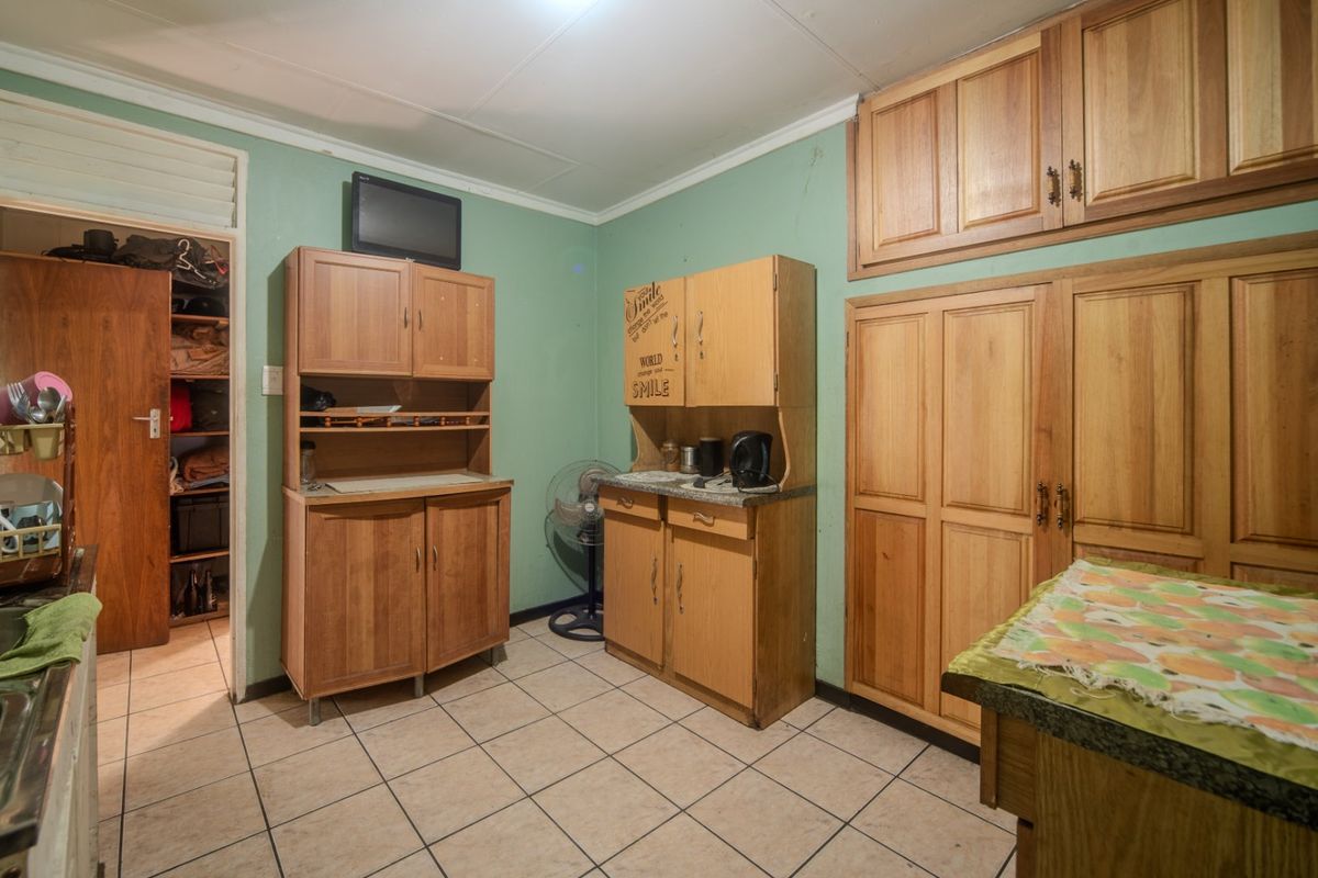 A dated kitchen featuring wooden cabinetry, tiled flooring, and a walk-in pantry, offering significant potential for a modern renovation.