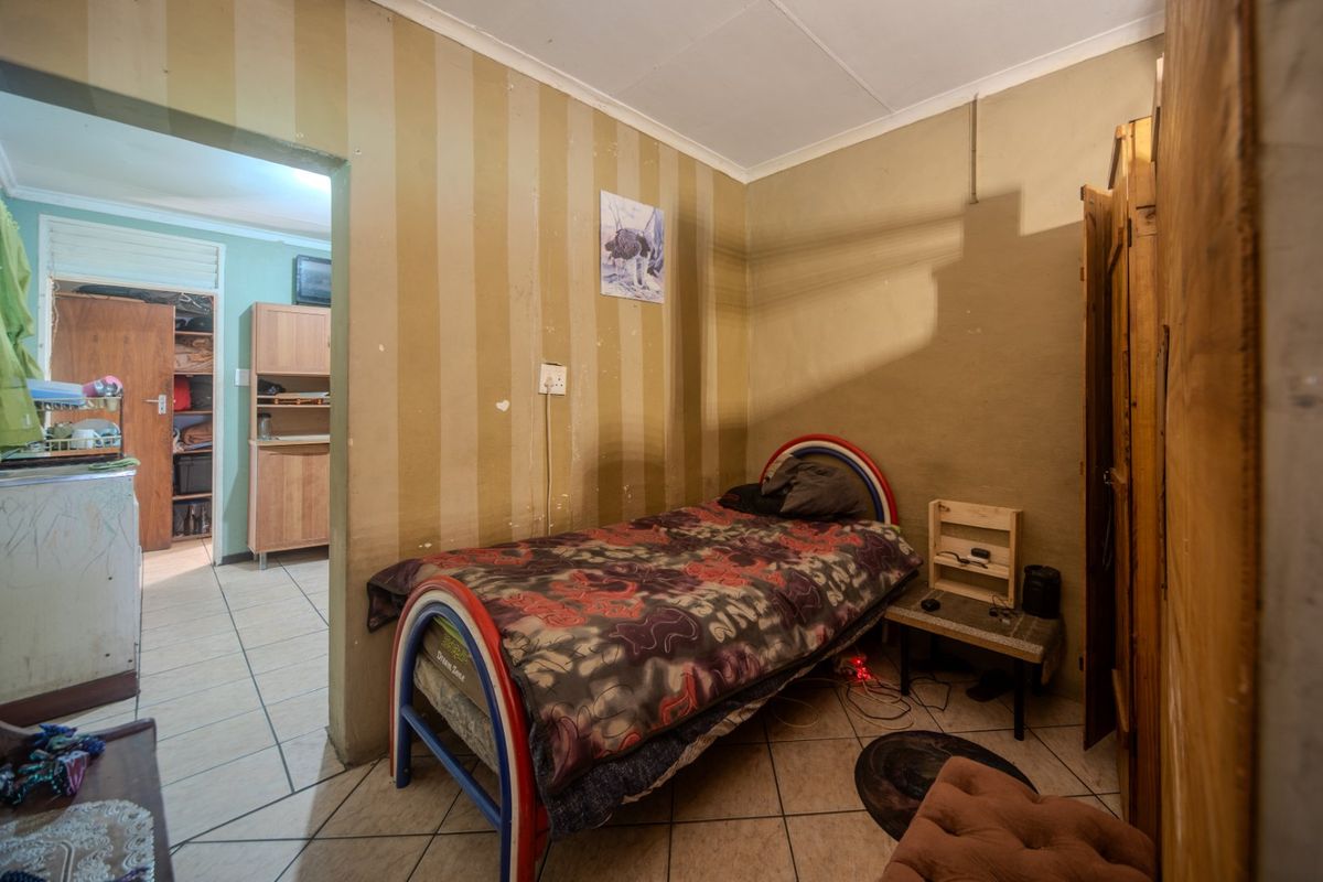 A bedroom featuring tiled flooring and a built-in cupboard, showing signs of wear and requiring cosmetic updates to the wall finishes.