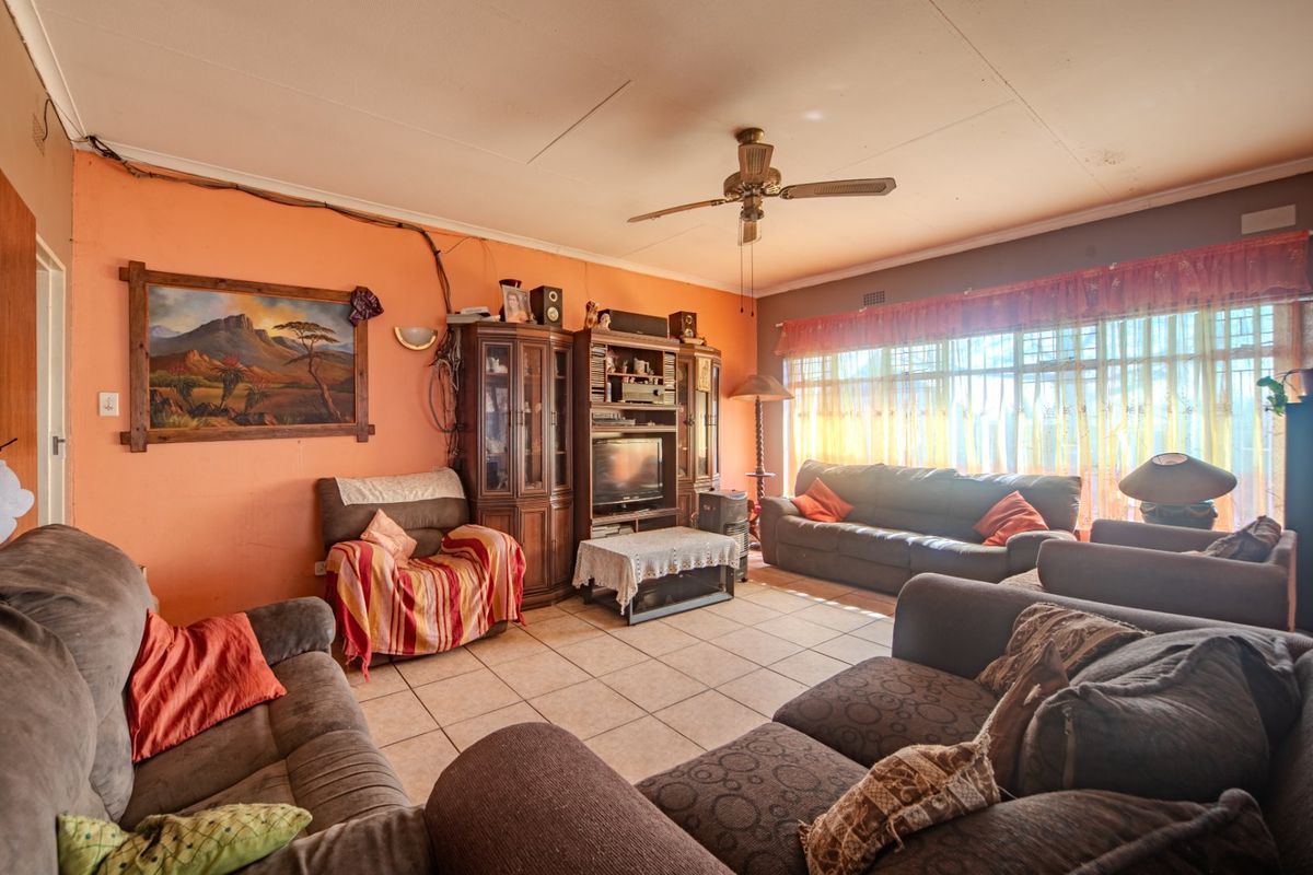 Spacious living room featuring tiled flooring, a ceiling fan, and large windows, offering a functional layout with potential for cosmetic updates.