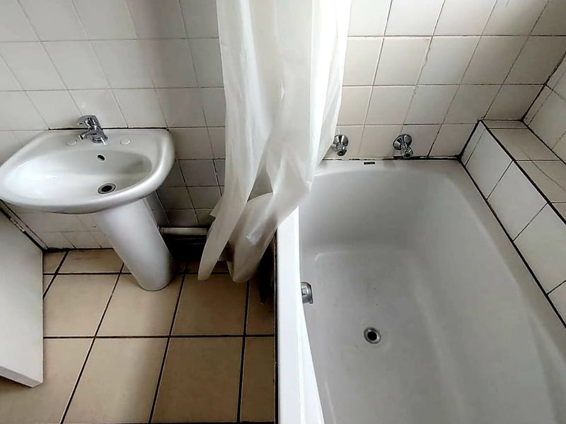 A functional bathroom featuring a white pedestal washbasin and a standard bathtub with tiled walls and flooring.