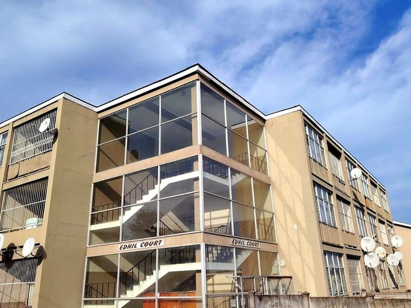 Exterior view of Ednil Court apartment building featuring a prominent glass-enclosed stairwell and multi-level residential units with security bars.