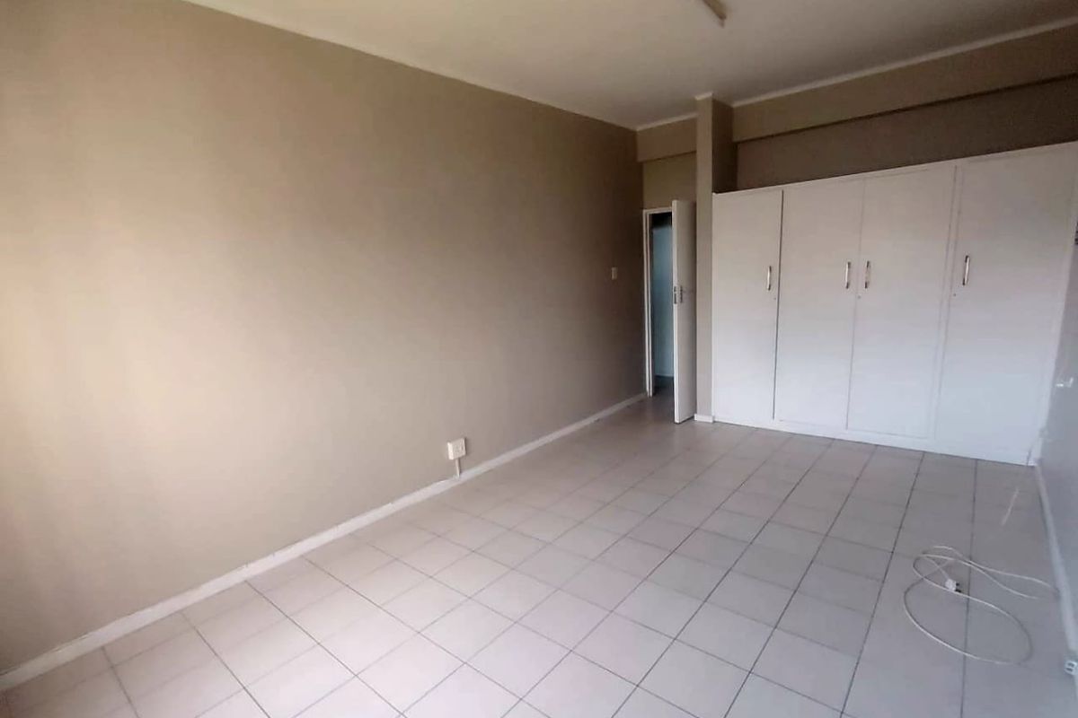 A spacious, empty bedroom featuring neutral wall tones, tiled flooring, and built-in white cupboards providing ample storage space.