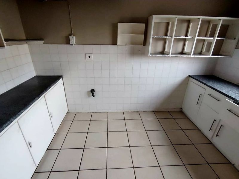 A dated, empty kitchen featuring tiled splashbacks, laminate countertops, and built-in cabinetry, offering a blank canvas for renovation and modernization.