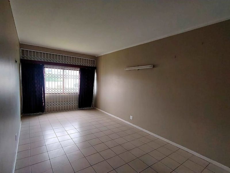 An empty living room featuring tiled flooring, a security gate on the window, and a wall-mounted light fixture.