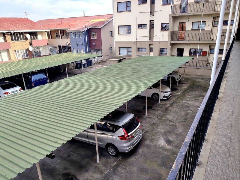 An elevated view of an apartment complex parking area featuring covered carport bays with corrugated metal roofing and concrete paving.