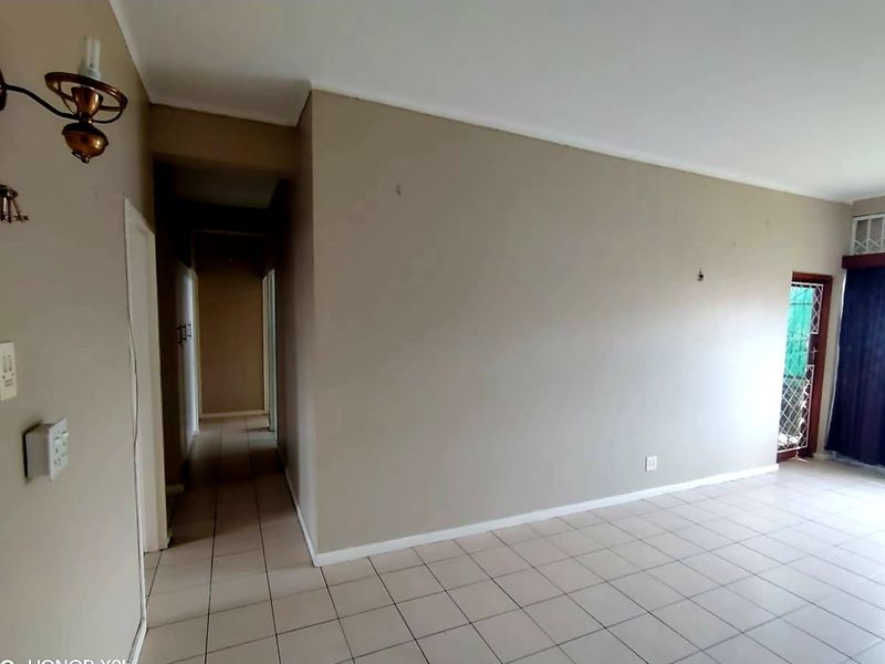 An empty living room featuring neutral wall tones, tiled flooring, and access to an outdoor area through a security gate and sliding door.