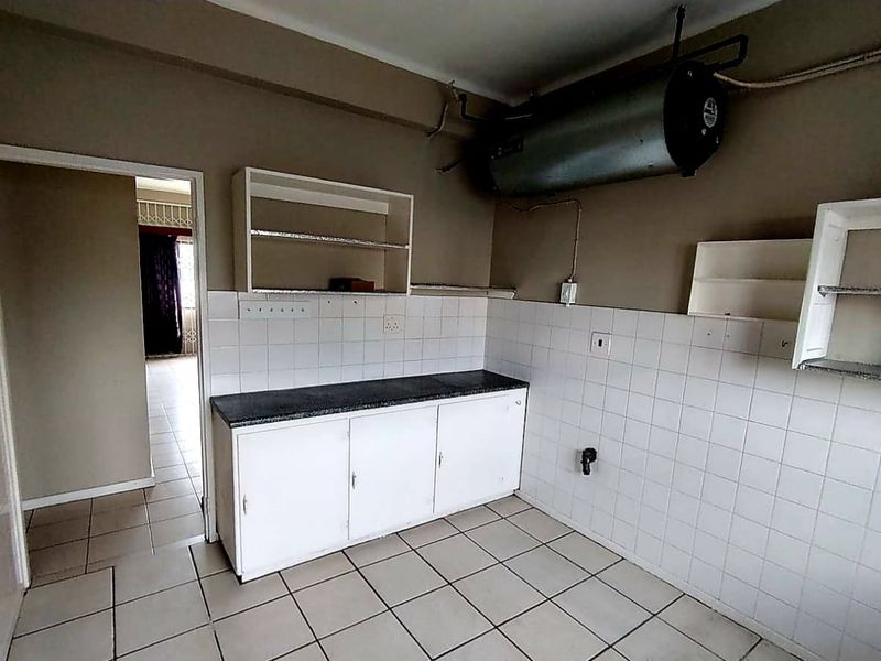 A basic kitchen area featuring tiled flooring, a tiled splashback, built-in base cabinetry, and an exposed wall-mounted electric water heater.