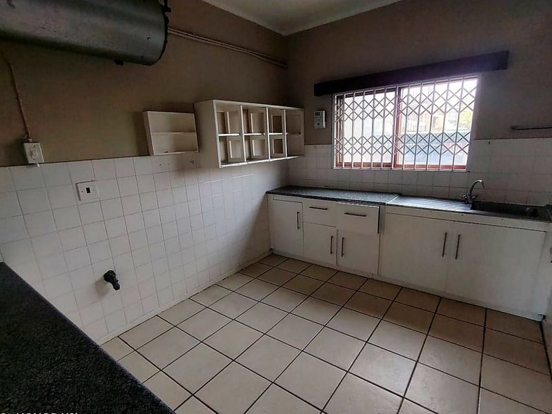 A functional kitchen space featuring built-in cabinetry, tiled splashbacks, and a stainless steel sink, offering a blank canvas for modern renovation.