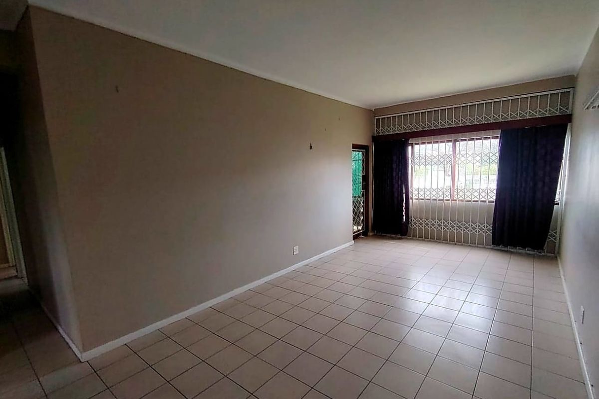 An empty living room featuring neutral ceramic floor tiles, large windows with security bars, and a security gate leading to the exterior.