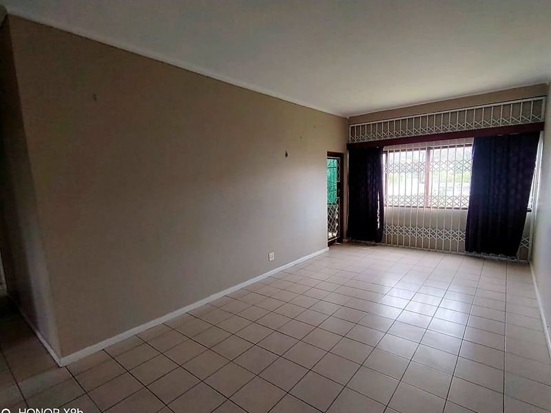 An empty living room featuring neutral ceramic floor tiles, large windows with security bars, and a security gate leading to the exterior.