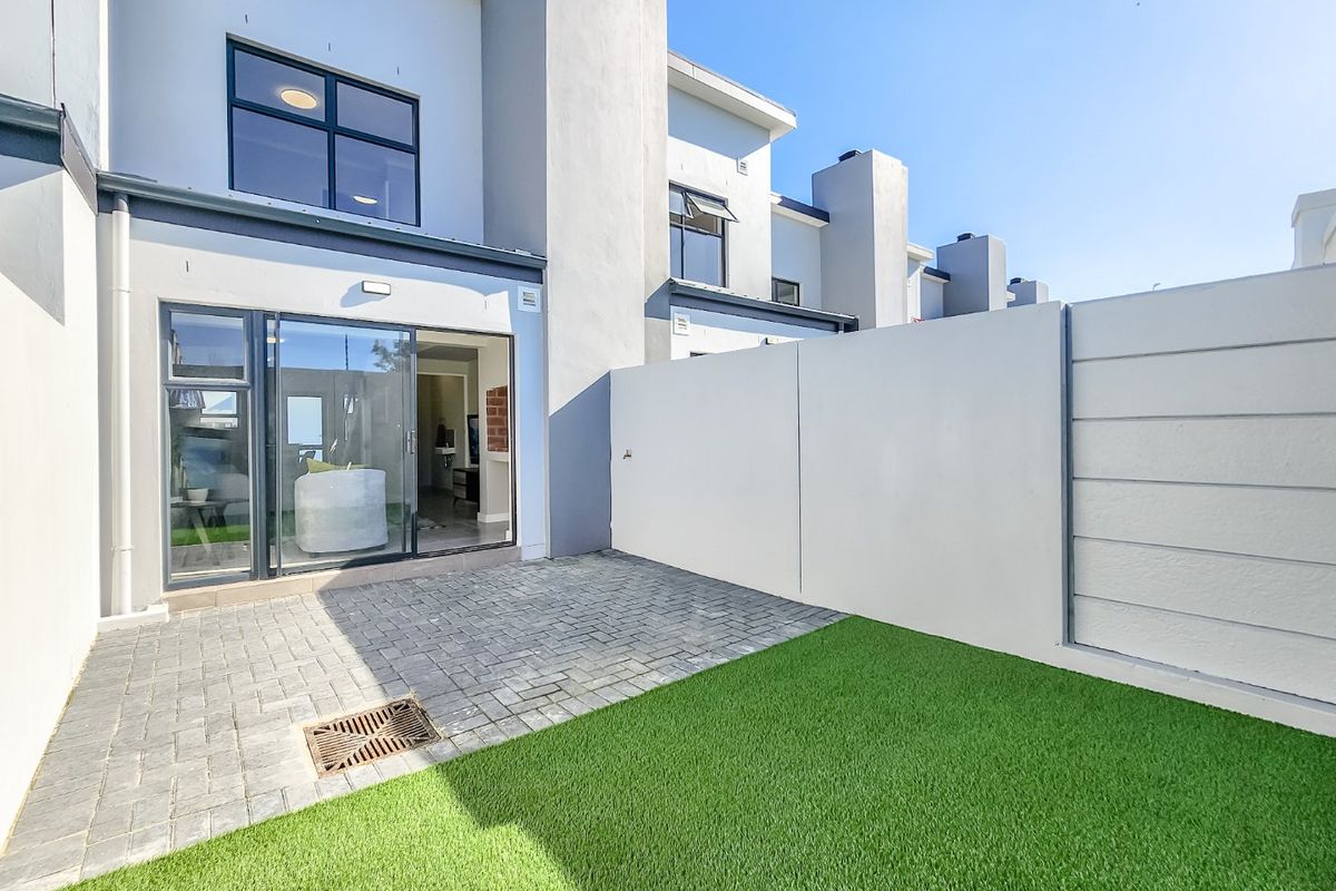 A well-maintained rear courtyard featuring a paved patio area, artificial lawn, and a secure boundary wall, providing direct access to the interior living space.