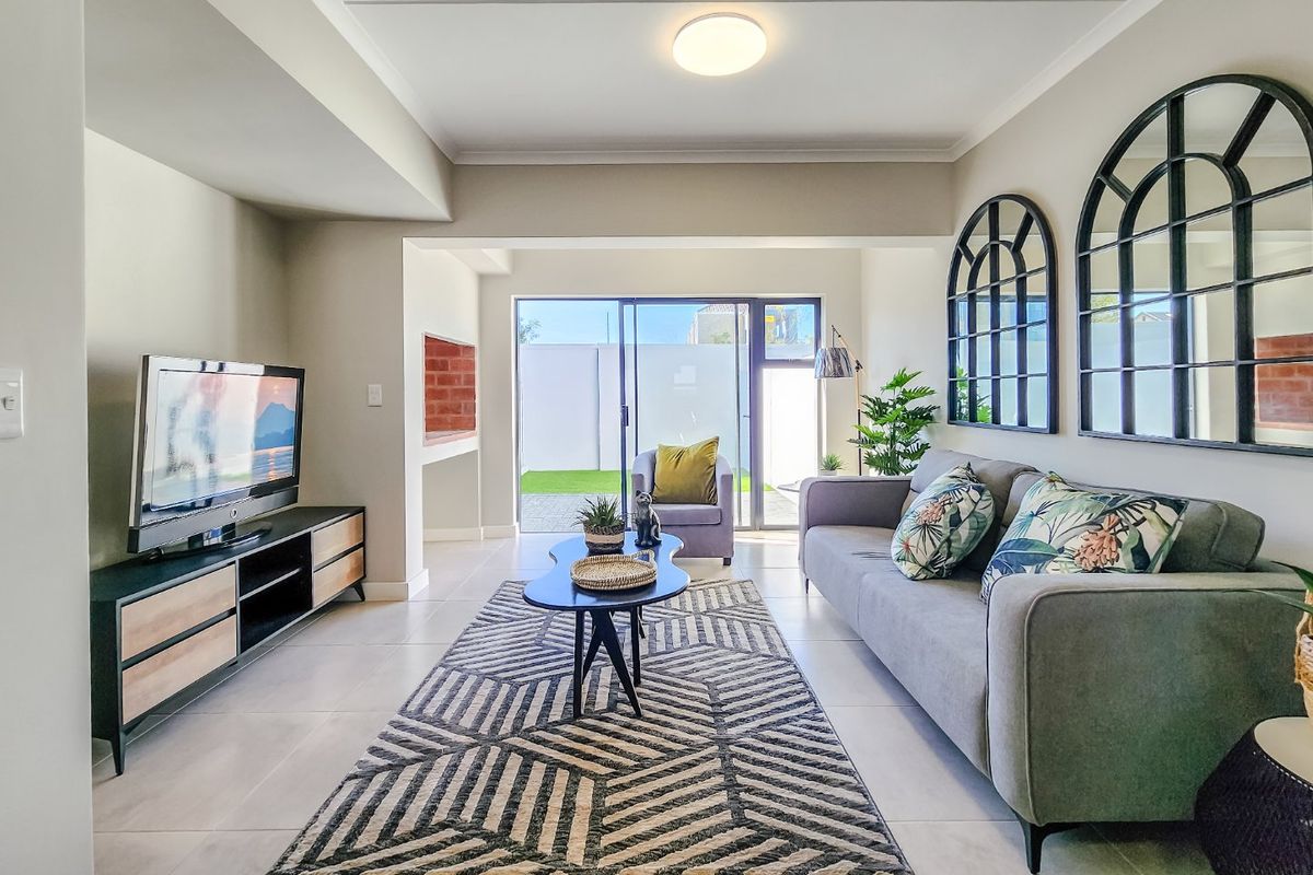 A bright and modern living room featuring tiled floors, a built-in indoor braai, and large sliding doors providing direct access to the rear garden.
