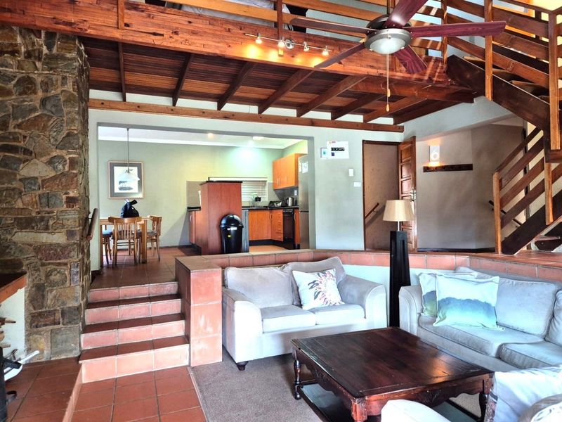 Open-plan living area featuring exposed timber beams, a stone fireplace wall, terracotta tiling, and an integrated kitchen with timber cabinetry.